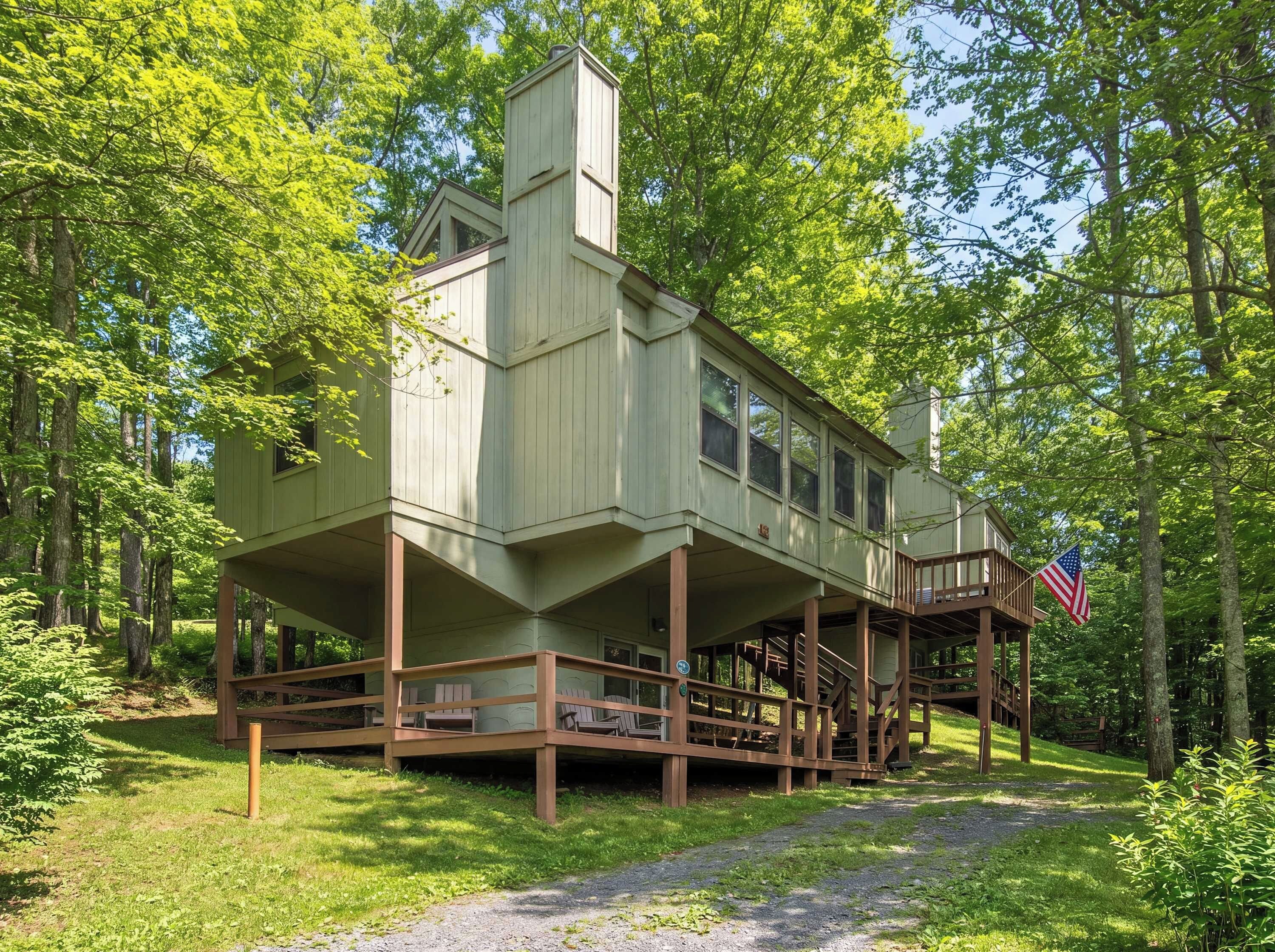 A cabin with a wooden deck and a flag, surrounded by trees.