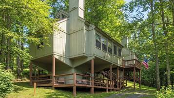 A cabin with a wooden deck and a flag, surrounded by trees.