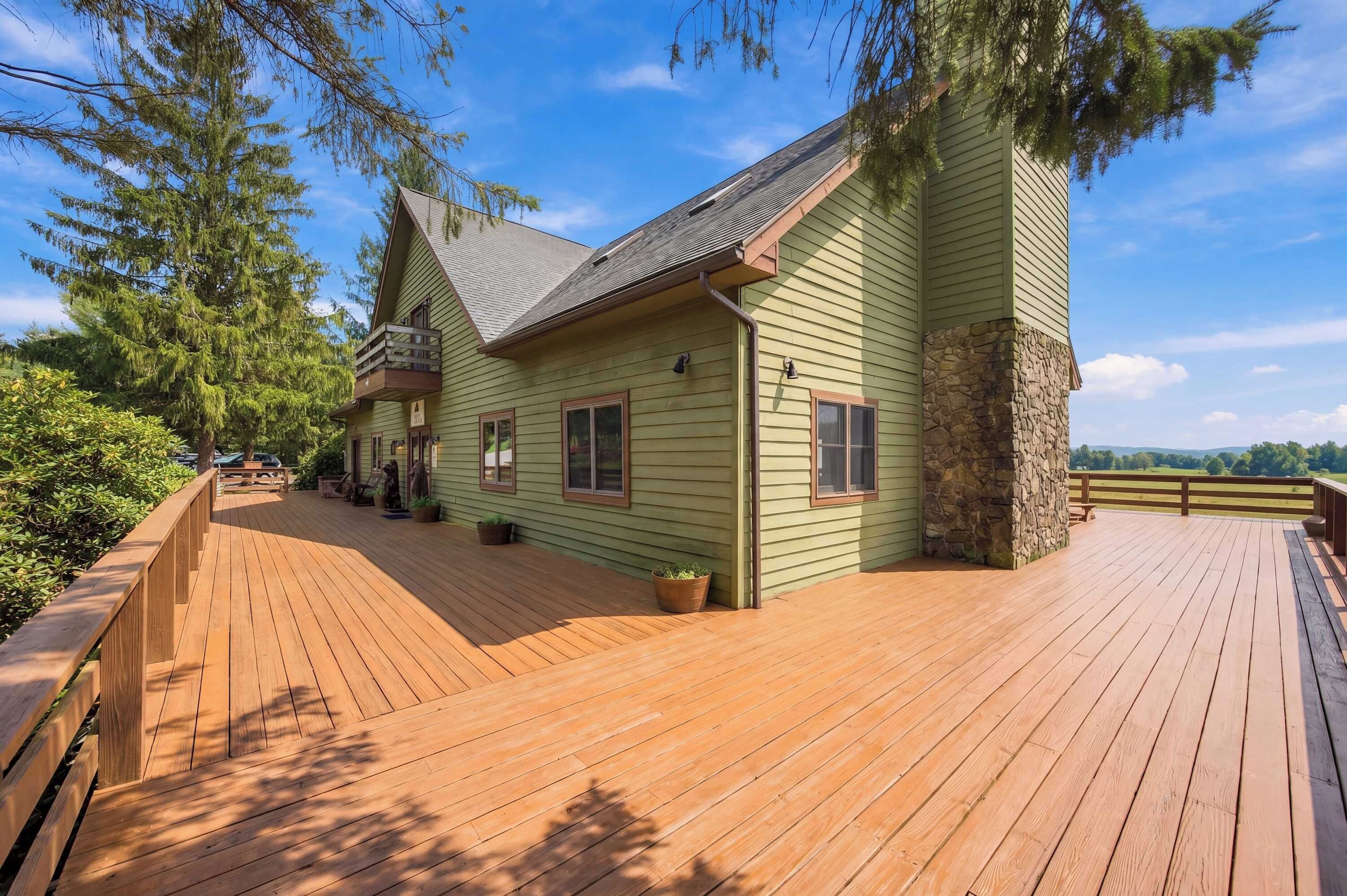 A green wooden house with a stone foundation, a wooden deck, and a clear view of the surrounding landscape.