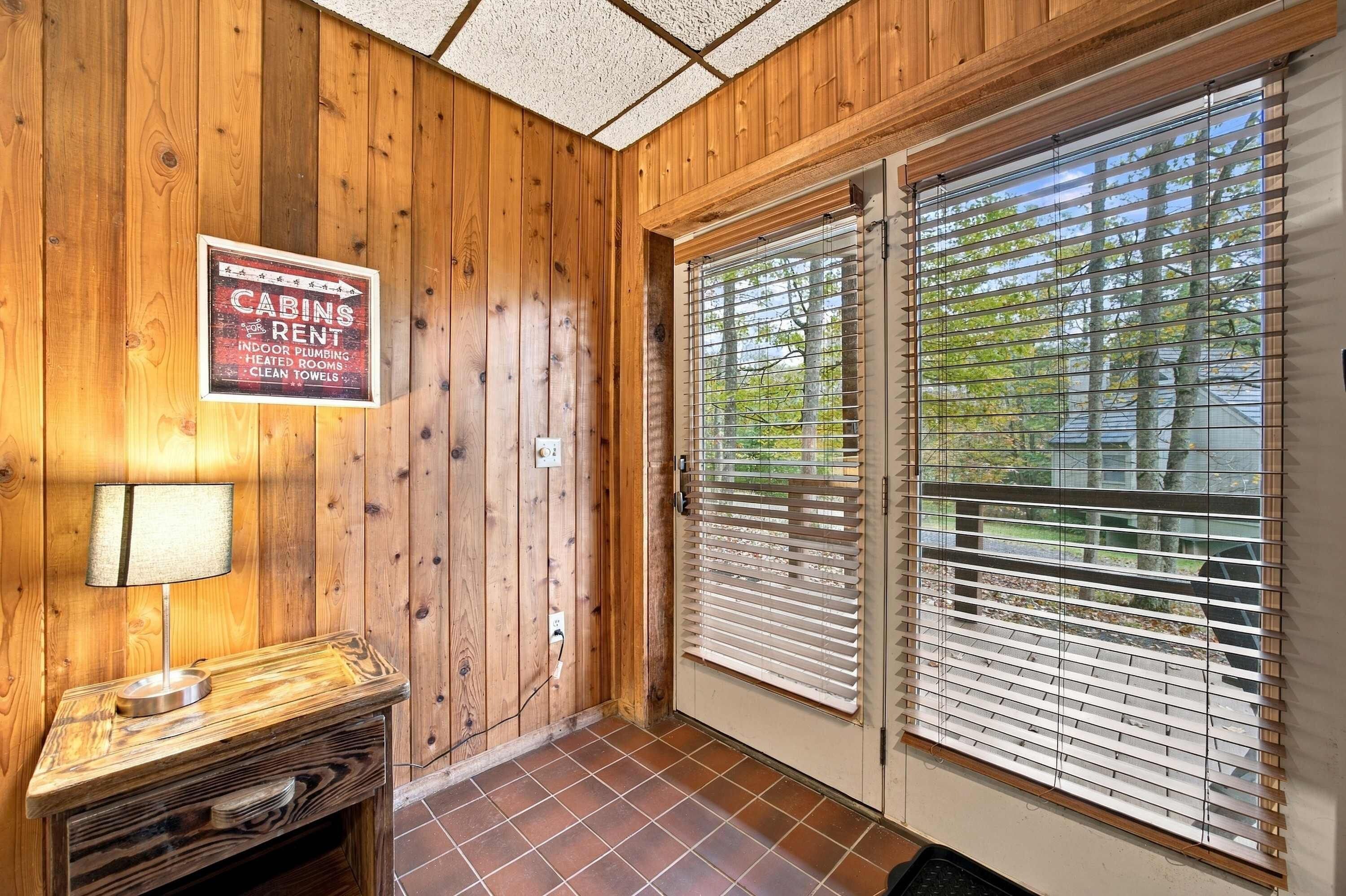 A cabin interior with wooden walls, a sign for rent, a lamp, and a door with blinds.