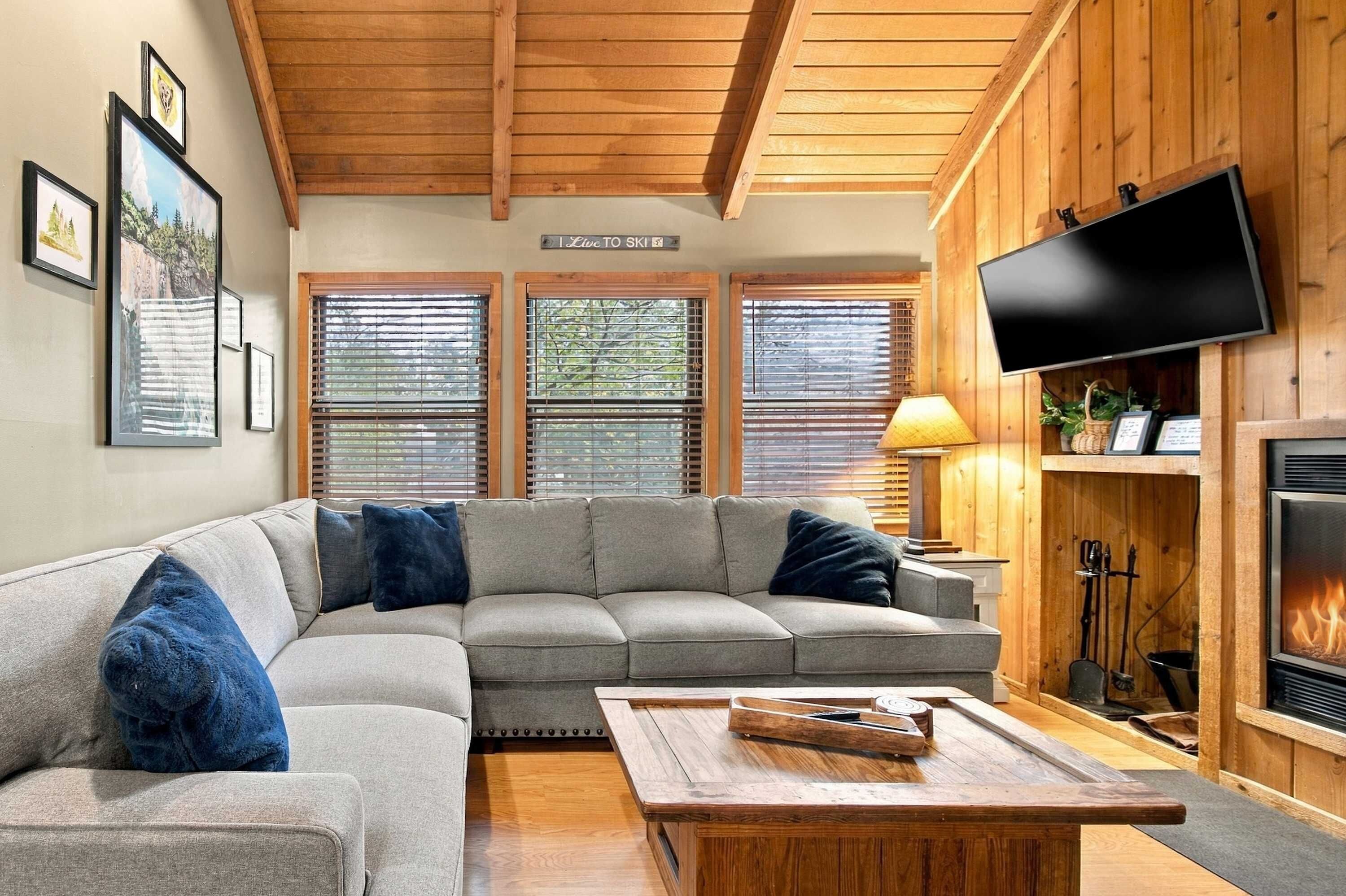 A cozy living room with a sectional sofa, a flat-screen TV, a fireplace, and framed pictures on the wall.