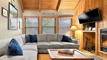 A cozy living room with a sectional sofa, a flat-screen TV, a fireplace, and framed pictures on the wall.