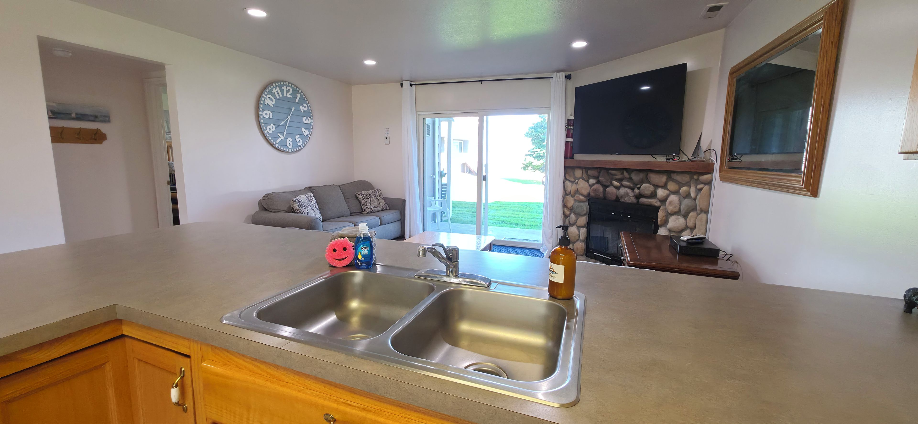A modern kitchen with a double sink, a stone fireplace, and a large window.