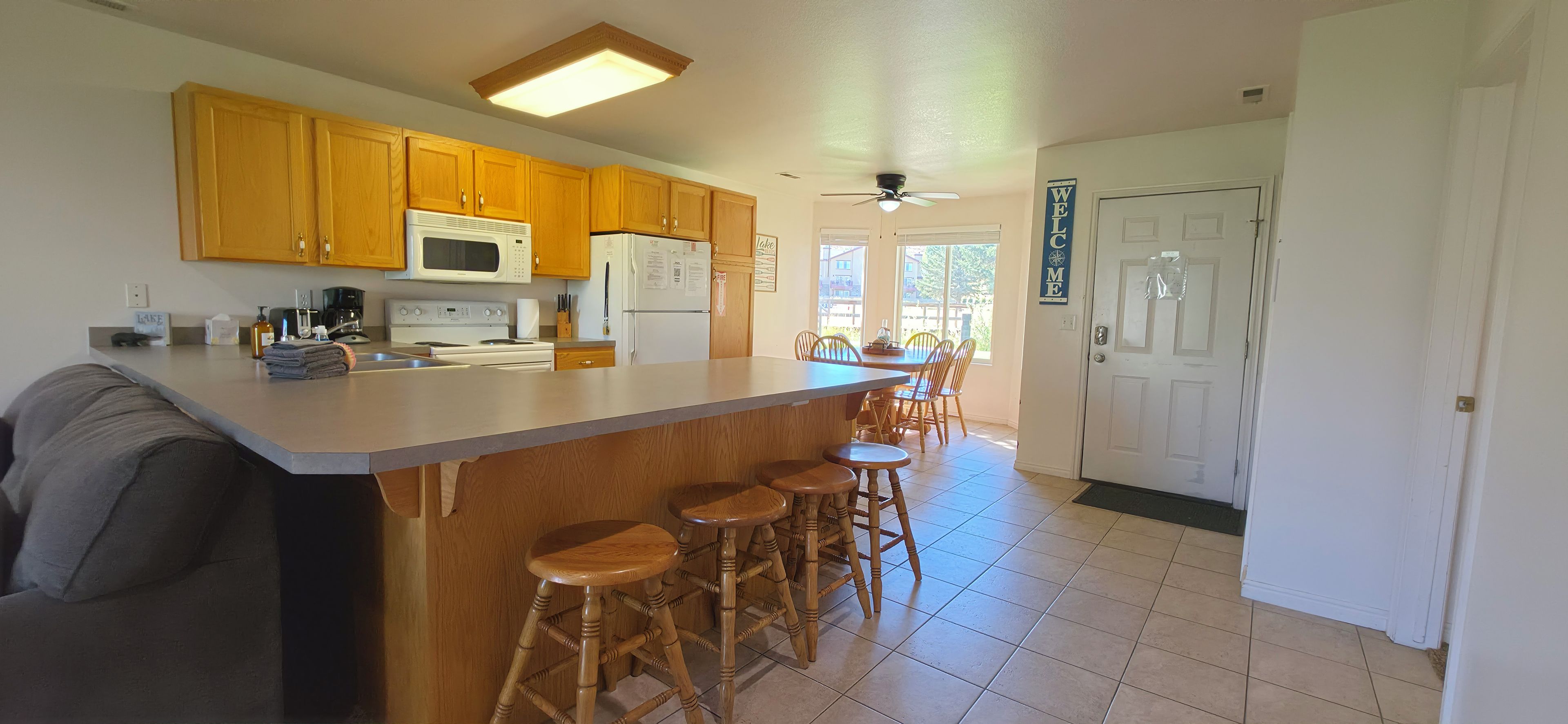 Una cocina con armarios de madera, microondas, refrigerador, estufa y una barra con taburetes.