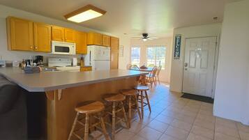 Una cocina con armarios de madera, microondas, refrigerador, estufa y una barra con taburetes.