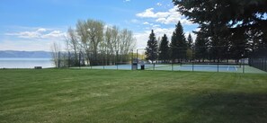 Un court de tennis avec un filet, entouré d’une clôture, et une étendue d’eau en arrière-plan.