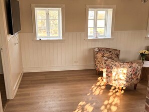 A room with two windows, wooden flooring, and a floral-patterned chair. - 6 Person Holiday Home in Blavand (Blavand)