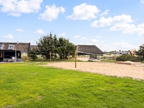 A beach volleyball court with a net, a grassy area, and a building with a thatched roof in the background. - 6 Person Holiday Home in Blavand (Blavand)