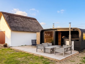 A thatched-roof building with an openable section revealing a fireplace, outdoor seating, and a wooden deck. - 6 Person Holiday Home in Blavand (Blavand)