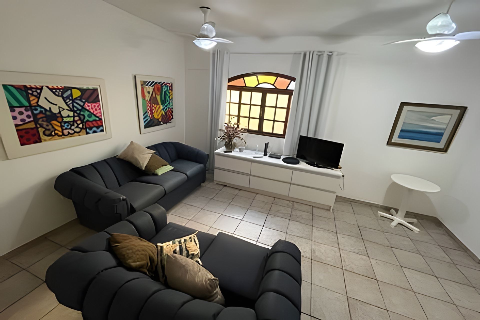 Una sala de estar con un sofá modular, un televisor de pantalla plana, una mesita y obras de arte en las paredes.