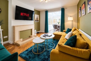 Ein Wohnzimmer mit Kamin, einer Couch, einem Couchtisch und einem Fernseher, der 'NETFLIX' anzeigt.