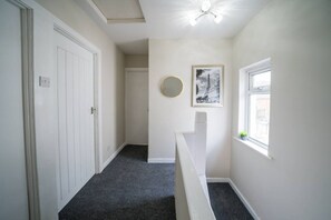 Ein Korridor mit einer weißen Tür, einer Treppe, einem gerahmten Bild an der Wand und einem Fenster mit Blick.