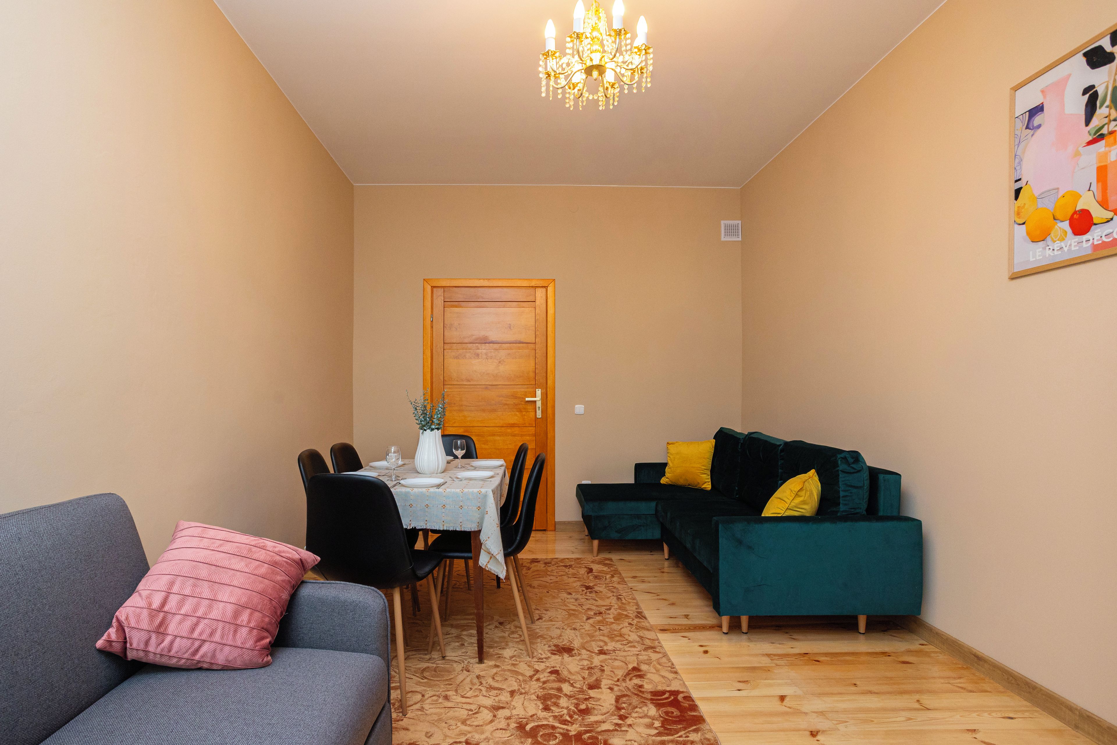 A living room with a dining area, a chandelier, a door, and a poster on the wall.