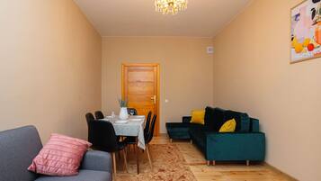 A living room with a dining area, a chandelier, a door, and a poster on the wall.