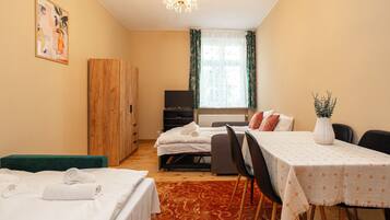A hotel room with two beds, a dining table, a TV, a wardrobe, and a window with curtains.