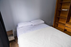 Ein Einzelbett mit weißer Bettwäsche in einem Zimmer mit hellgrauen Wänden und einem Holzschrank.