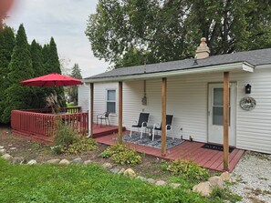 A single-story house with a covered porch, a red umbrella, and a welcome sign.