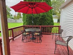 A red deck with a round table and chairs, a red umbrella, and a white building in the background.