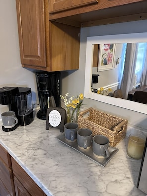 A kitchen counter with a coffee maker, mugs, a tray, and a basket.