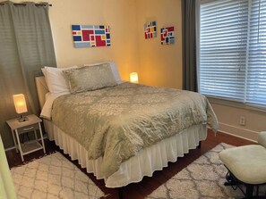 Quarto com cama, luminárias de cabeceira, tapete e quadros na parede.