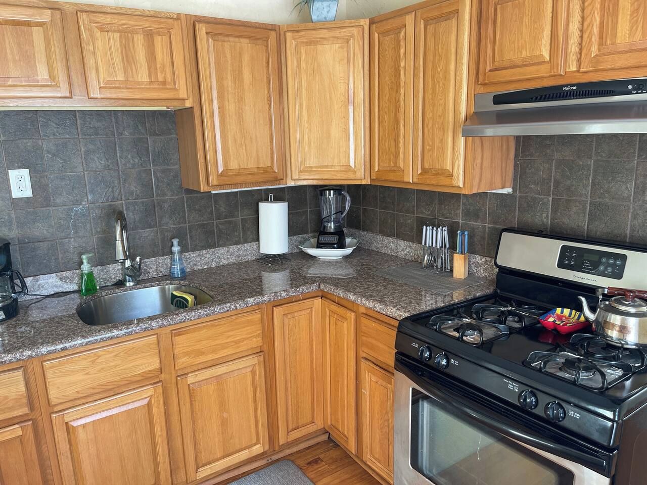 A kitchen with wooden cabinets, a granite countertop, a stainless steel sink, a coffee maker, and a stove.