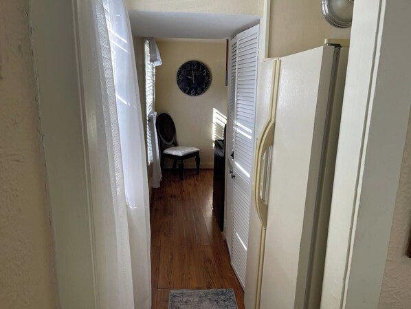 Um corredor estreito com piso de madeira, uma porta branca e um relógio fixado na parede.