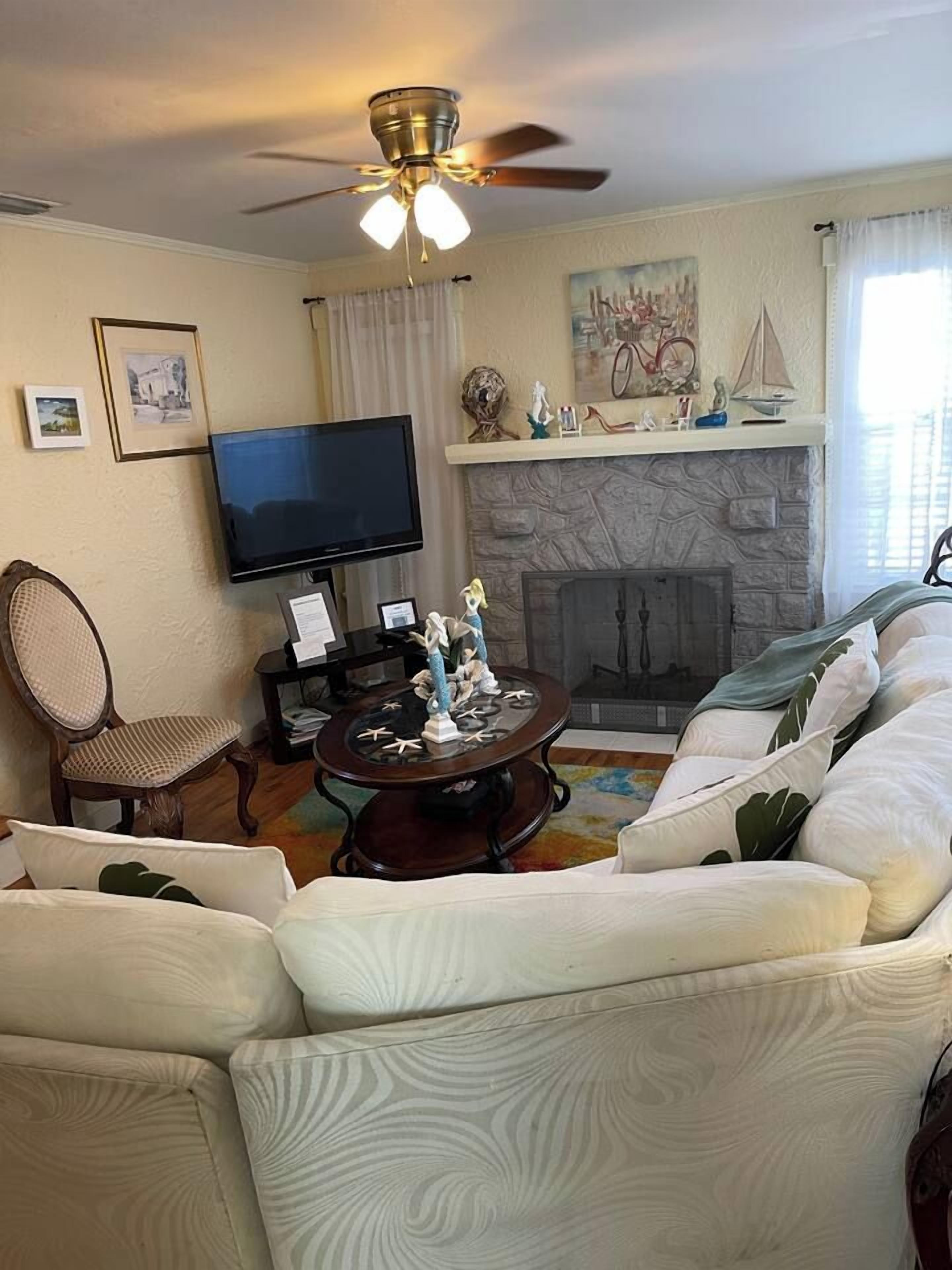 Un salon avec un canapé, un téléviseur, une cheminée et un ventilateur de plafond.