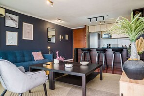 Een moderne woonkamer met een bank, salontafel en een keukenhoek met barstoelen.
