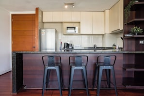 A kitchen with a wooden door, a built-in microwave, a stainless steel sink, and three bar stools. - Kennedy Apartments by Andes with Parking (Santiago)
