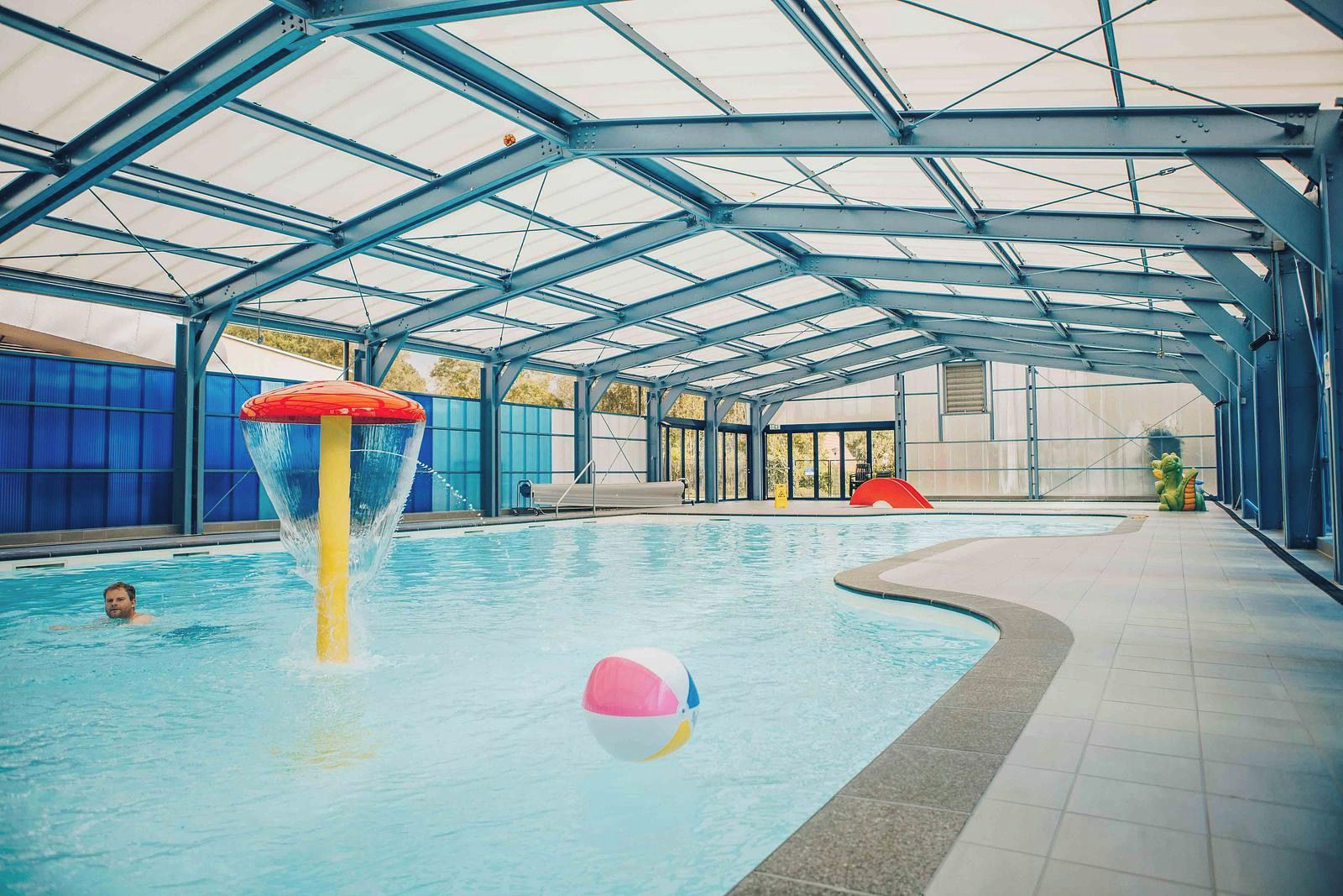 An indoor swimming pool with a covered roof, a water slide, and a beach ball.
