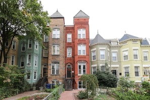 A row of multi-story buildings with distinct architectural styles, including a red brick building with a tower, a green building with ornate detailing, and a yellow building with a gabled roof. - Private English Basement apartment nestled in Shaw (Washington)