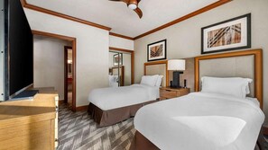 Quarto de hotel com duas camas, uma escrivaninha, televisão e obras de arte nas paredes.
