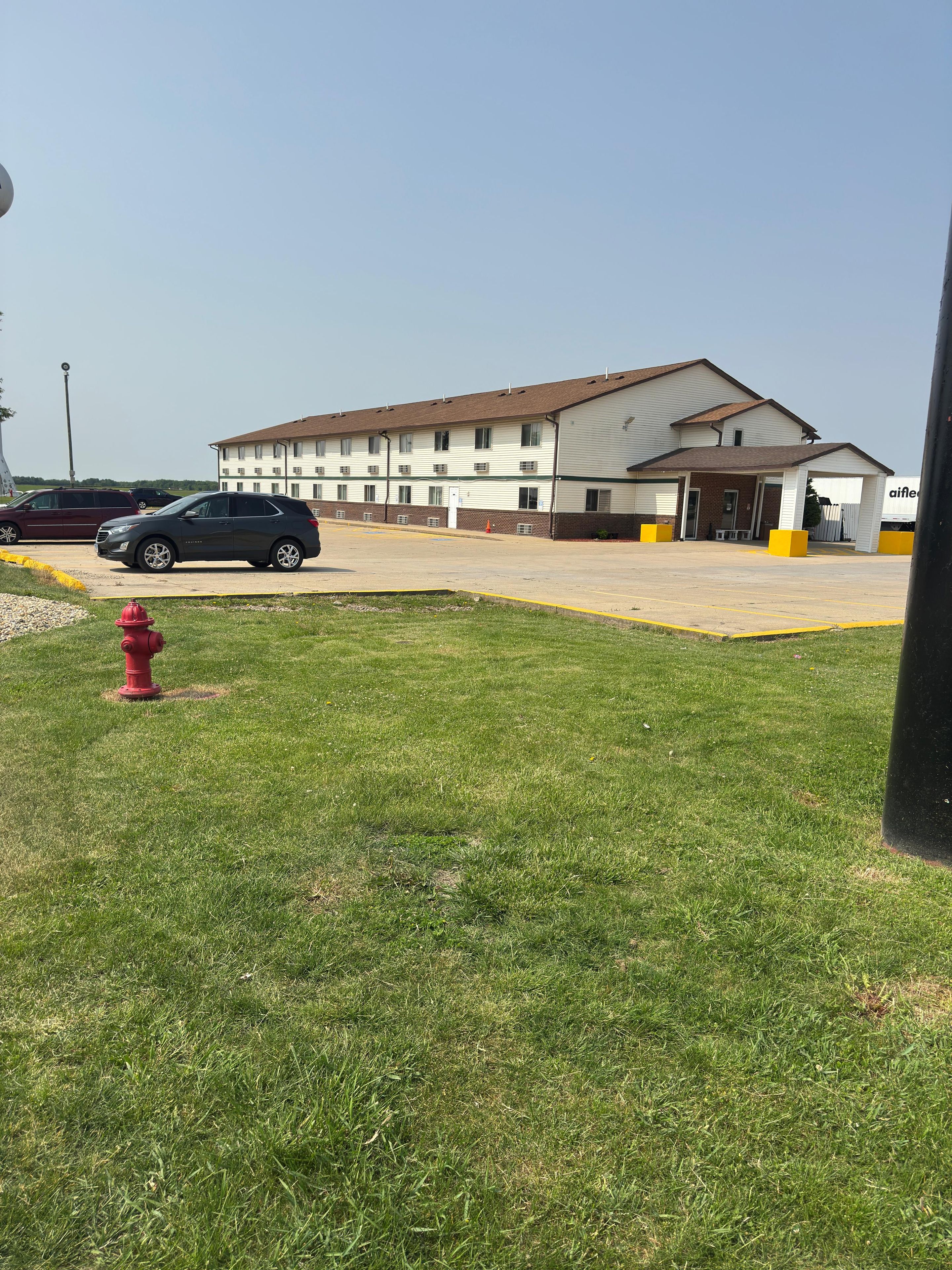 A multi-story motel with a parking lot, a red fire hydrant, and a large truck in the background.