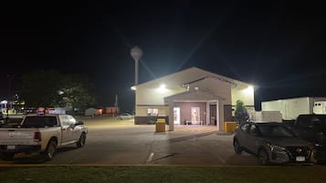 Un edificio con vestíbulo cubierto, estacionamiento y un tanque de agua al fondo.
