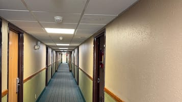 Un largo y estrecho pasillo de hotel con alfombra estampada, puertas a ambos lados y un detector de incendios en el techo.