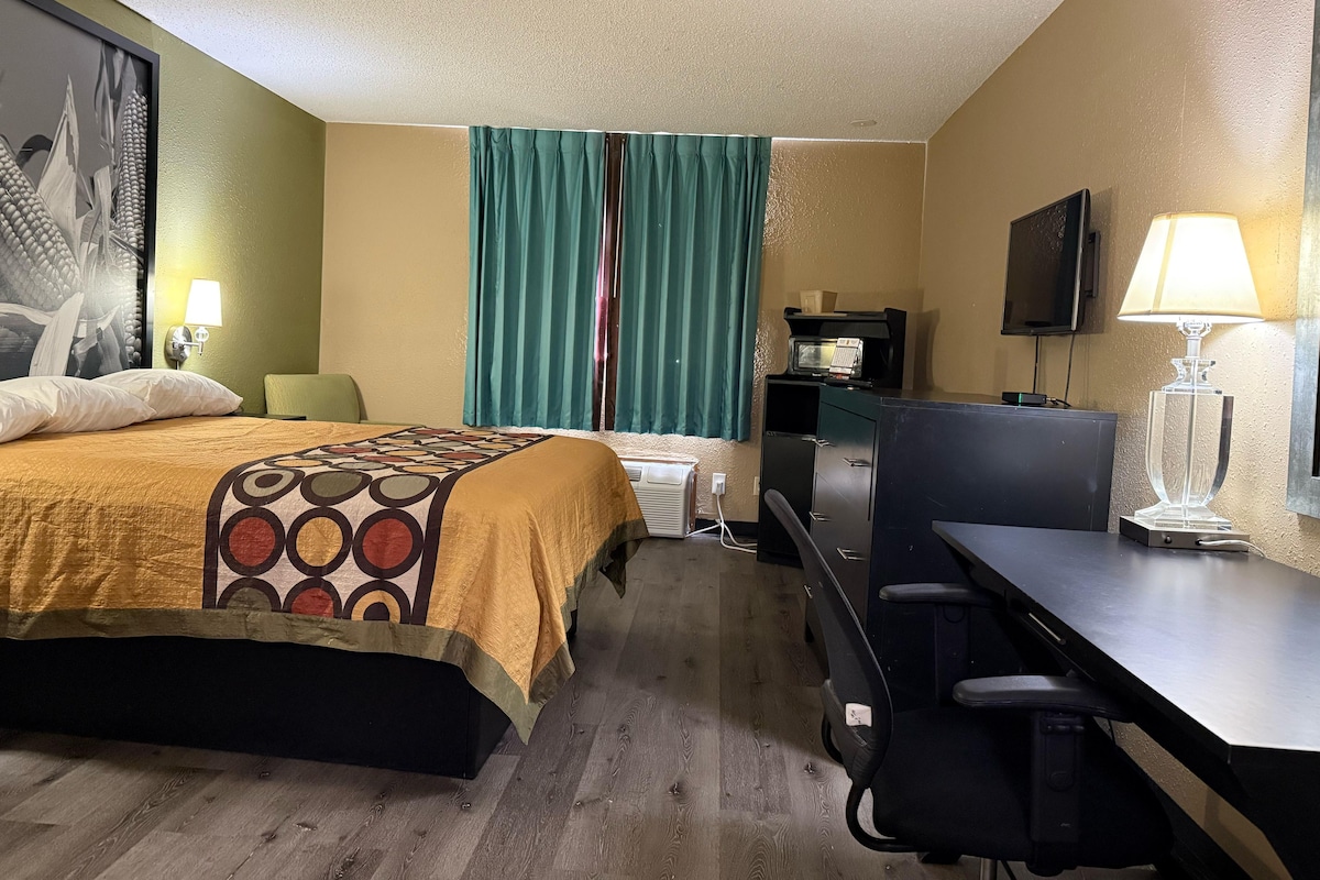 A hotel room with a bed, a desk, a chair, a television, and a window with curtains.