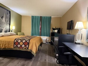 Habitación de hotel con cama, escritorio, silla, televisión y ventana con cortinas.