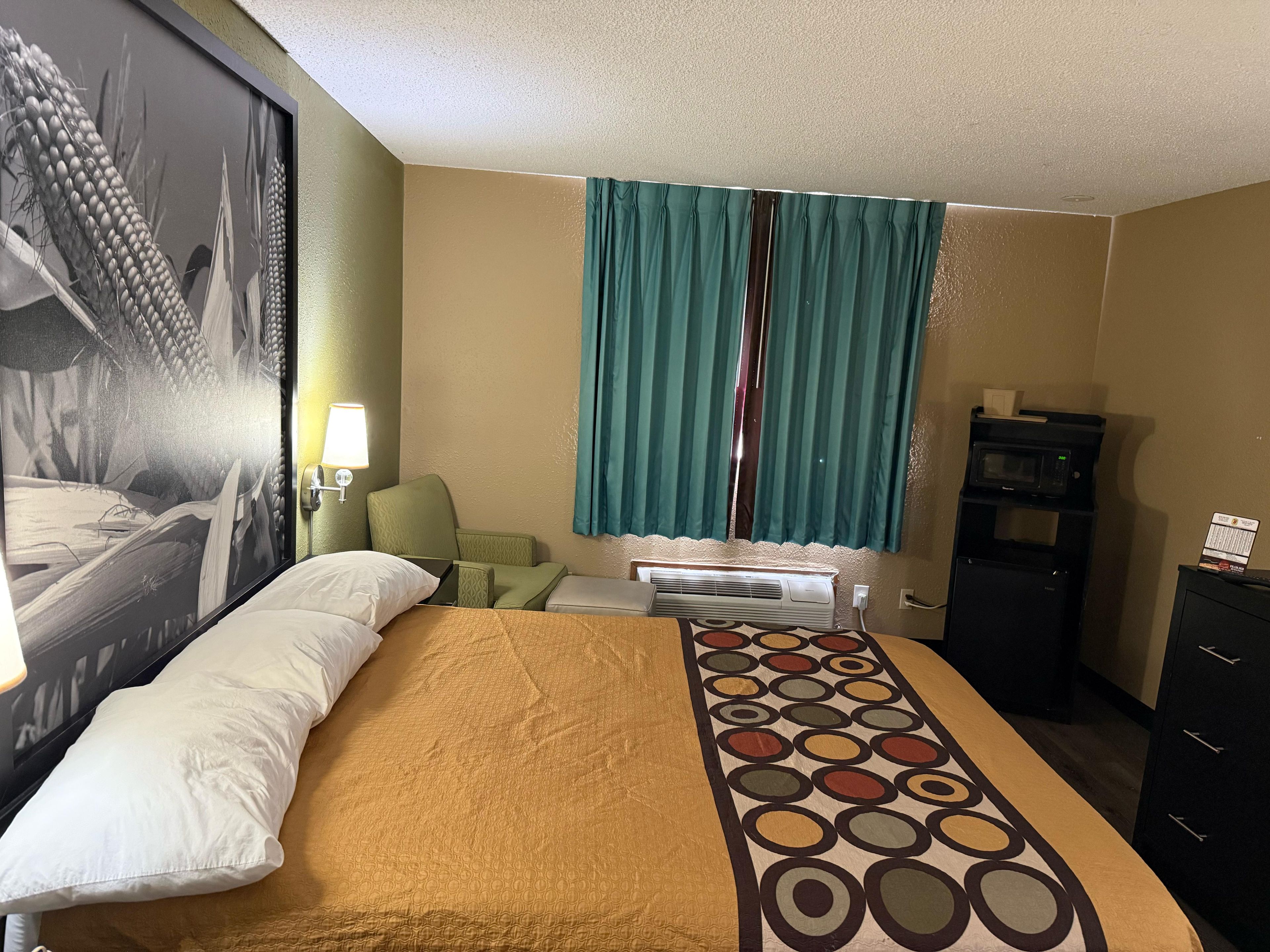 A hotel room with a bed, a desk, a chair, a microwave, and a dresser.