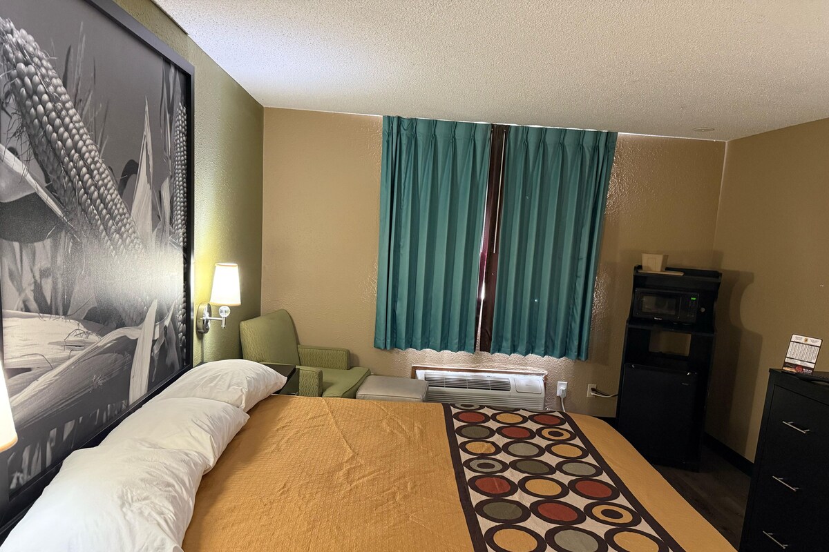 Una habitación de hotel con cama, escritorio, silla, microondas y cómoda.