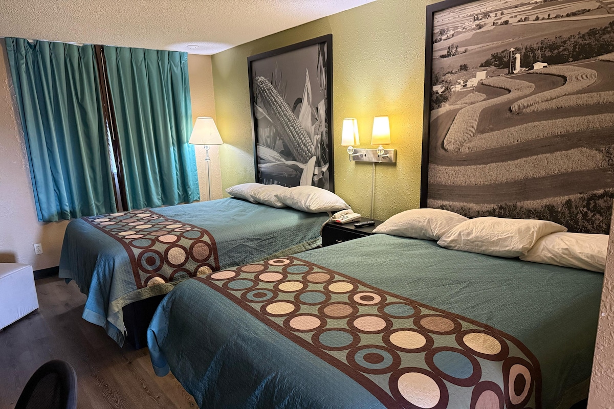 Een hotelkamer met twee bedden, een nachtkastje met een lamp, een telefoon en een lijst met een foto aan de muur.