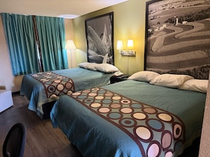 Een hotelkamer met twee bedden, een nachtkastje met een lamp, een telefoon en een lijst met een foto aan de muur.