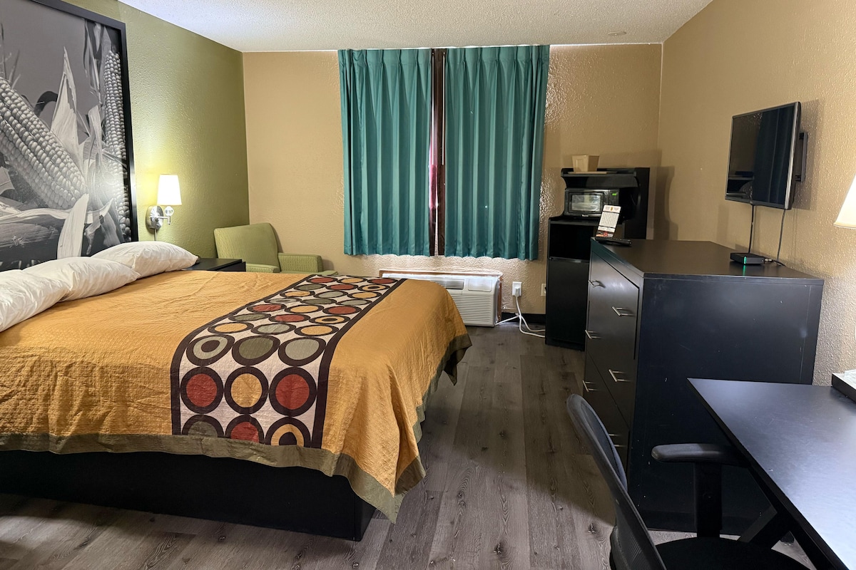 A hotel room with a bed, a desk, a chair, a TV, a microwave, and a small refrigerator.
