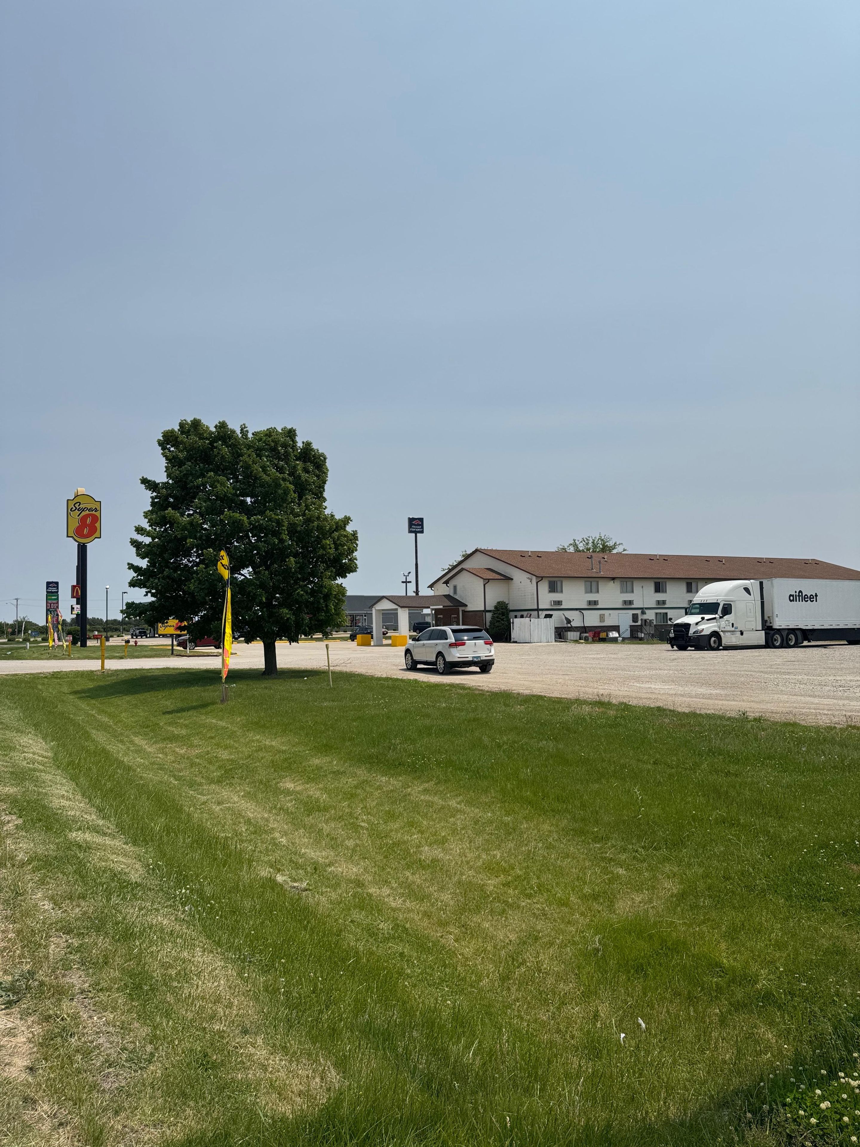 A parking lot with a white truck and a white car, a large tree, and a building with a flat roof.