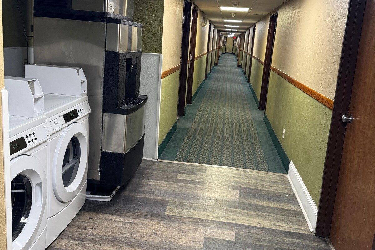 Un pasillo de hotel con lavadora, kitchenette y una larga galería con puertas a ambos lados.