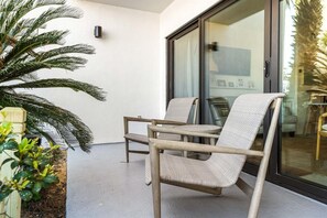 A balcony with two wicker chairs, a potted plant, and a sliding glass door leading to an interior space. - Emerald Hill 21 (Santa Rosa Beach)