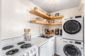 A compact kitchen with a stove, sink, and stacked appliances including a washing machine and dryer. - Emerald Hill 21 (Santa Rosa Beach)