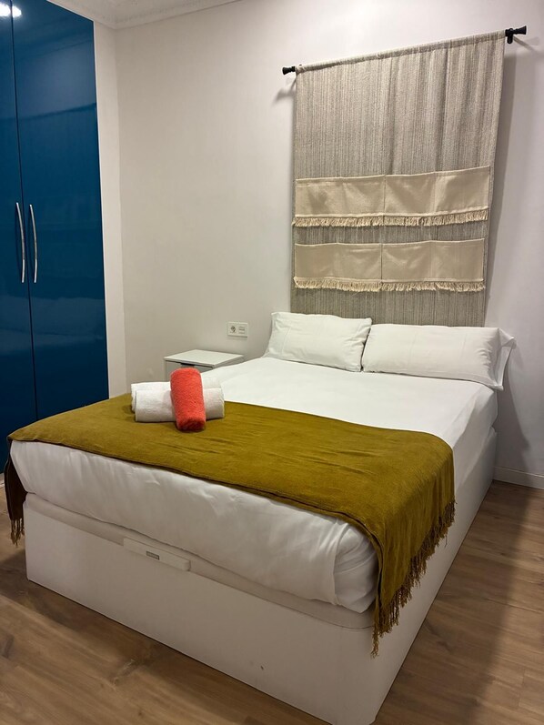 A bedroom with a bed, white bedding, a red and white towel, a green throw blanket, a blue wardrobe, and a wall-mounted curtain. - Vrbo Property (Donostia / San Sebastián)