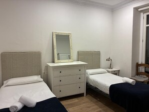 A hotel room with two single beds, a dresser with a mirror, a bedside table with a lamp, and a window with a view. - Vrbo Property (Donostia / San Sebastián)