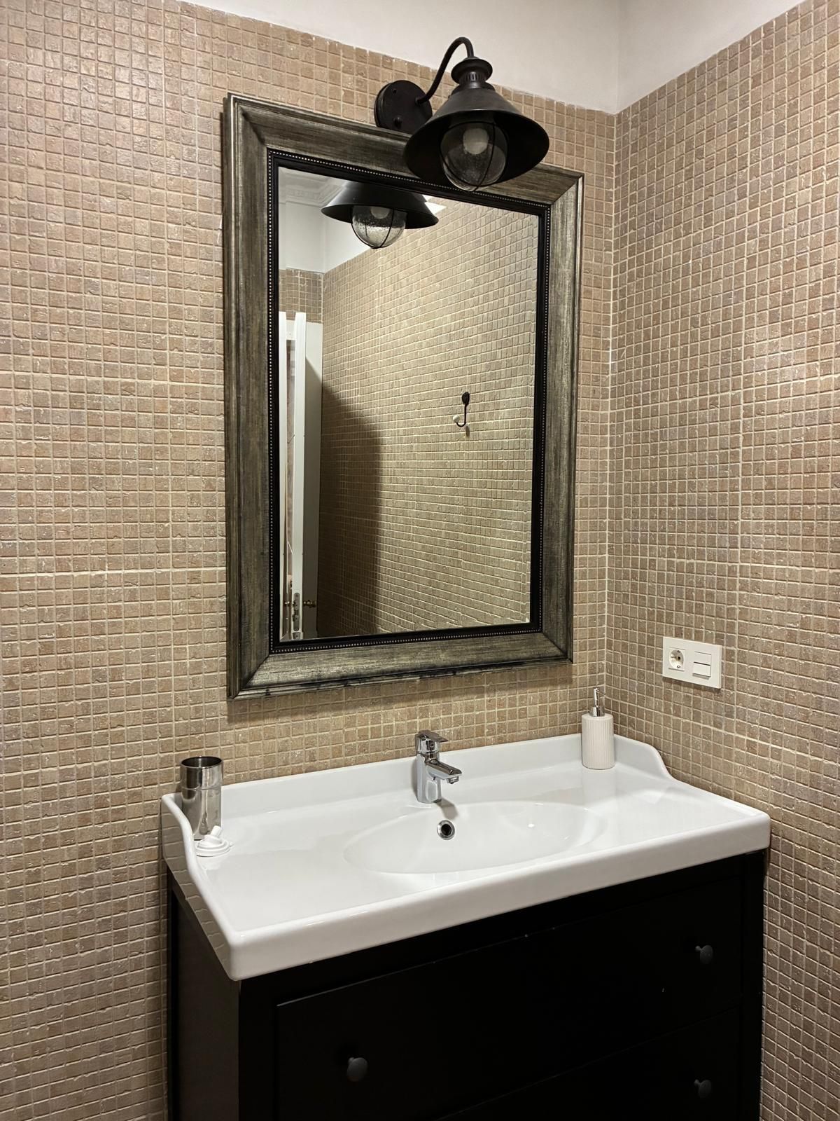 Un baño con un lavamanos blanco, un mueble negro debajo y un espejo con una lámpara de pared negra encima.