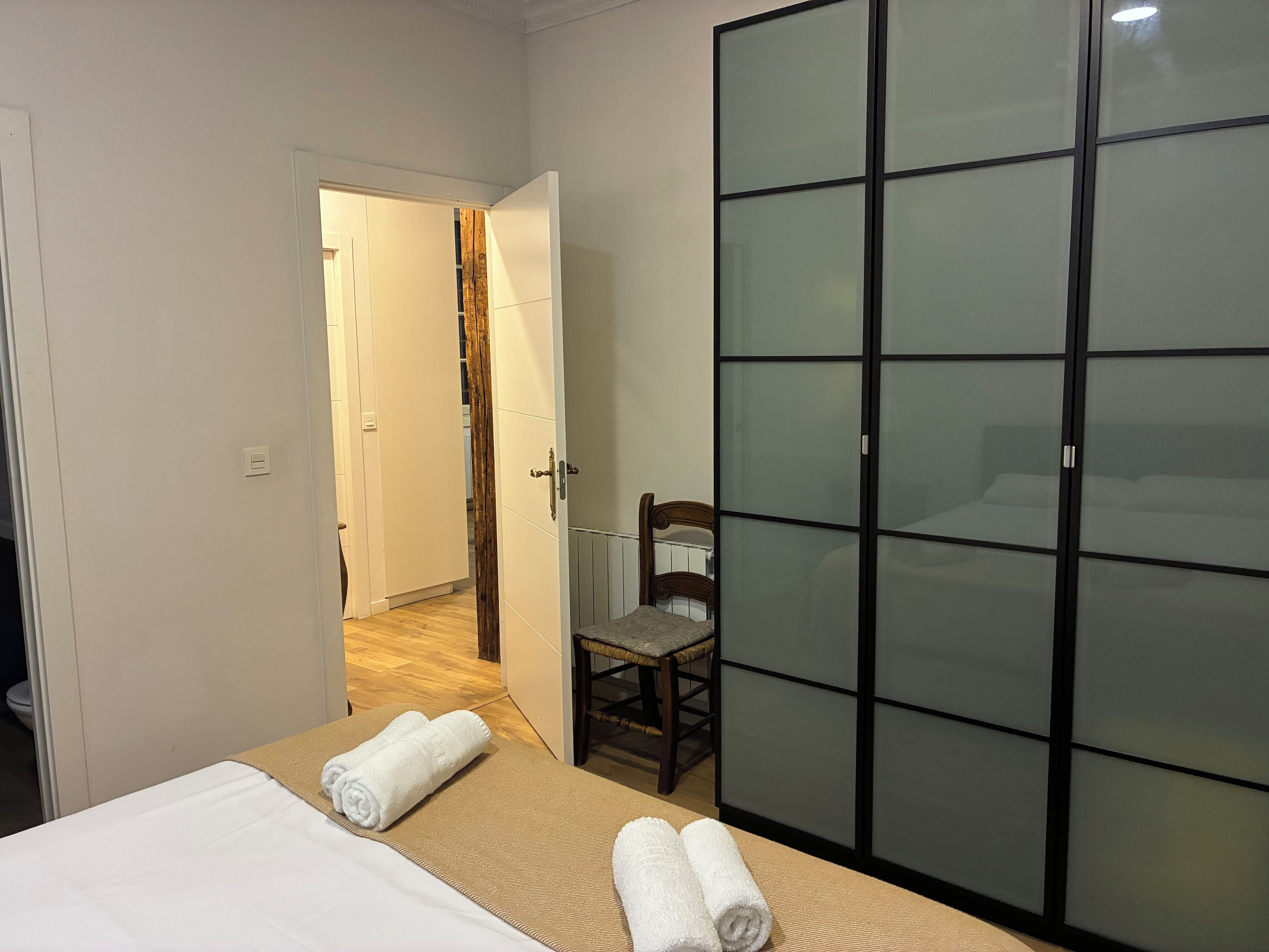 A hotel room with a bed, a chair, a wardrobe, and a door leading to another room.